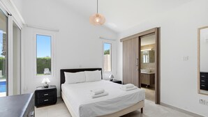 Une chambre à coucher comprenant un lit, des tables de chevet, une lampe, une vue sur l’extérieur, ainsi qu’une salle de bain avec un lavabo et un miroir.