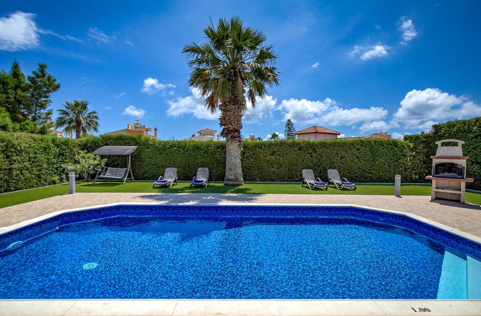 Una piscina con sillas de descanso, una palmera y una parrilla.