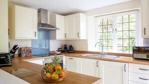 A modern kitchen with white cabinets, a stainless steel range hood, a built-in oven, a double sink, and a window with a view of greenery.