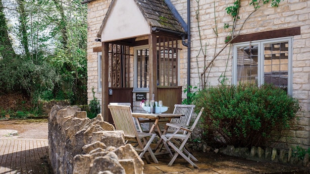 A stone building with a wooden porch, a table with chairs, and a sign reading "Emma Dent".