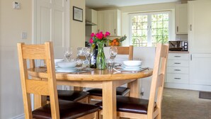 A dining area with a wooden table set for four, surrounded by wooden chairs with leather seats.