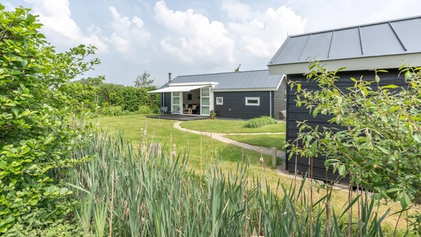 Ein modernes Haus mit überdachter Terrasse, gepflegtem Rasen und Garten.