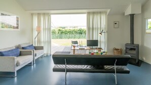 Ein Wohnzimmer mit einer Couch, einem Fernseher, einem Kamin und Blick ins Freie.