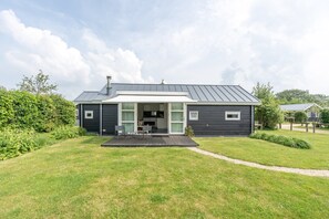 Une maison moderne à l’extérieur sombre, dotée d’un patio couvert et d’une pelouse bien entretenue.