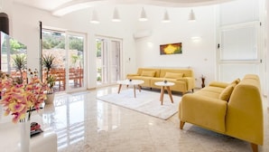 A spacious living room with a yellow sofa, two round tables, and a large window with a view of greenery. - Villa Anfiteatro Adriatico with Pool (Murter)