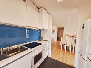Een moderne keuken met witte kasten, een blauwe spatwand, een ingebouwde oven en een eethoek met een witte tafel en stoelen.