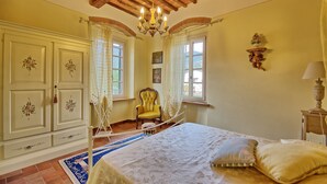 Ein Schlafzimmer mit Bett, Sessel, einer Chandelierleuchtre und einem Vorhangfenster.
