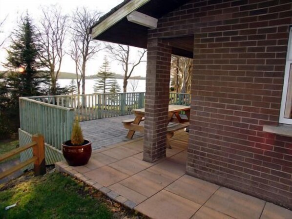 Un edificio de ladrillo con un patio cubierto, una terraza de madera y vistas a un lago.