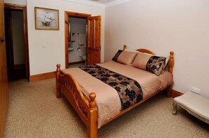 A bedroom with a wooden bed, a bedside table, and a door leading to a bathroom. - Cottage 173 - Clifden (Clifden)