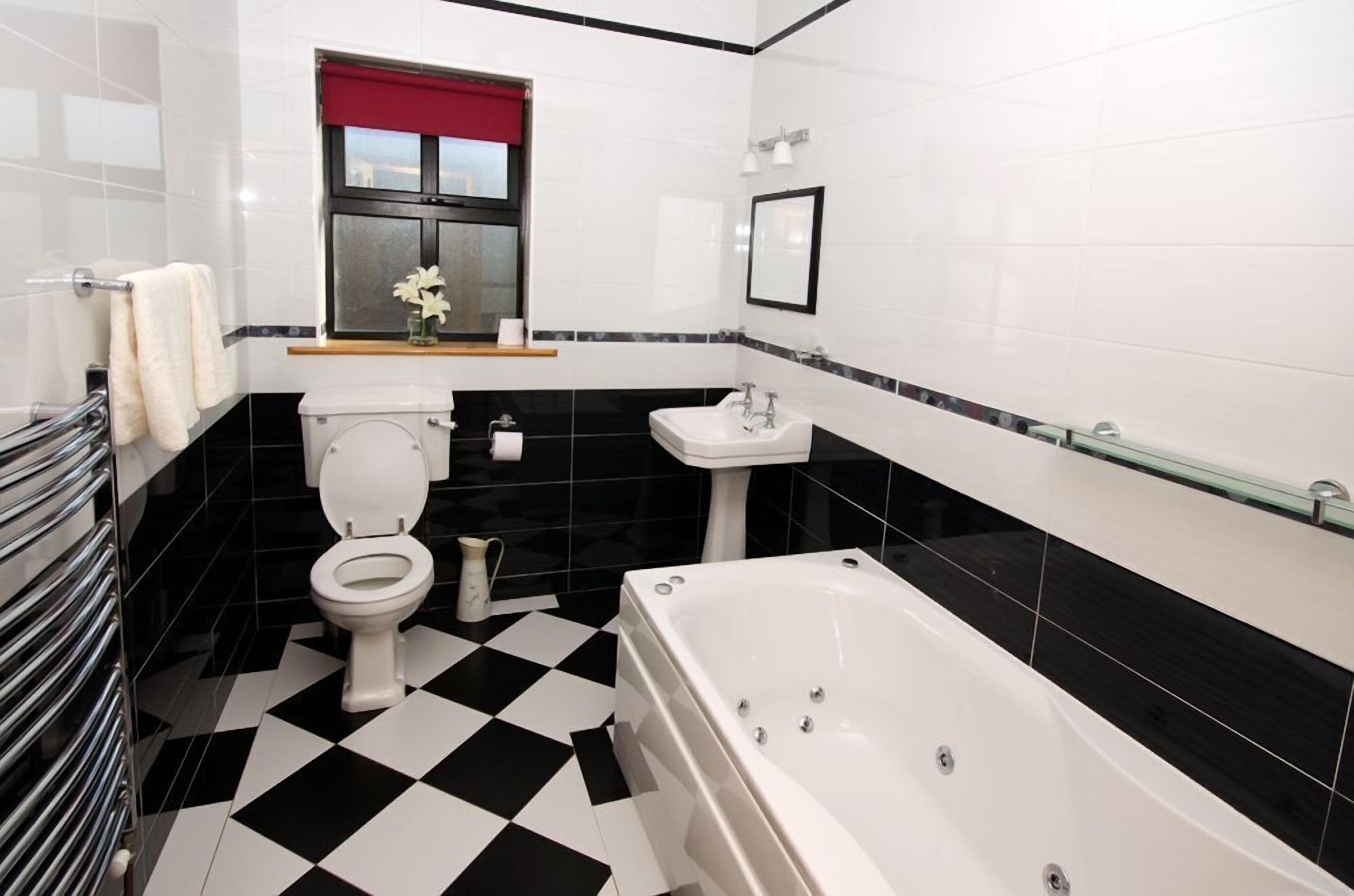 A bathroom with a black and white checkered floor, a white toilet, a white bathtub, a sink, and a window with a red blind.