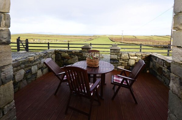 A stone-walled outdoor seating area with a round table and chairs, overlooking a rural landscape.