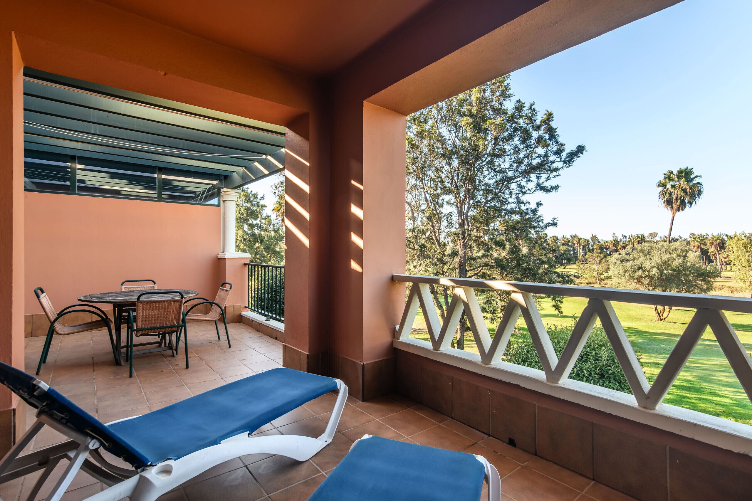 Un balcon avec une table et des chaises, deux fauteuils de relaxation et une vue sur un terrain de golf.