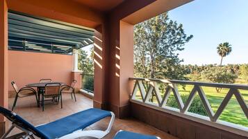 Un balcon avec une table et des chaises, deux fauteuils de relaxation et une vue sur un terrain de golf.