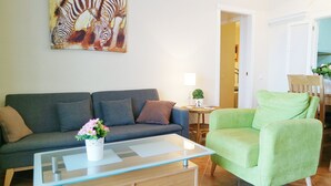 A living room with a grey sofa, a green armchair, a glass coffee table, and a painting of zebras on the wall.