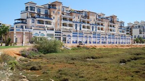 A multi-story hotel with balconies, a sandy ground in front, and a clear sky.