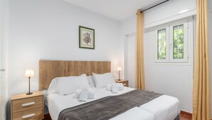 A neatly arranged hotel room with a bed, bedside tables, a nightstand, a window with curtains, and a wall-mounted picture. - Hoyo I - Isla Canela Golf GHHI15B2P65 (Isla Canela)