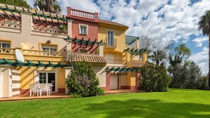 A two-story house with a patio, a dining area, and a well-maintained lawn. - Hoyo I - Isla Canela Golf GHHI15B2P65 (Isla Canela)
