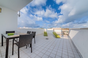 Une terrasse sur le toit, avec une table et des chaises, un fauteuil de jardin vert et une vue sur le paysage urbain.