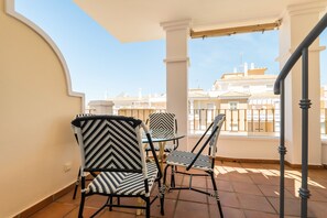 Un balcon avec deux chaises et une table, un sol carrelé et une vue sur les bâtiments en arrière-plan.