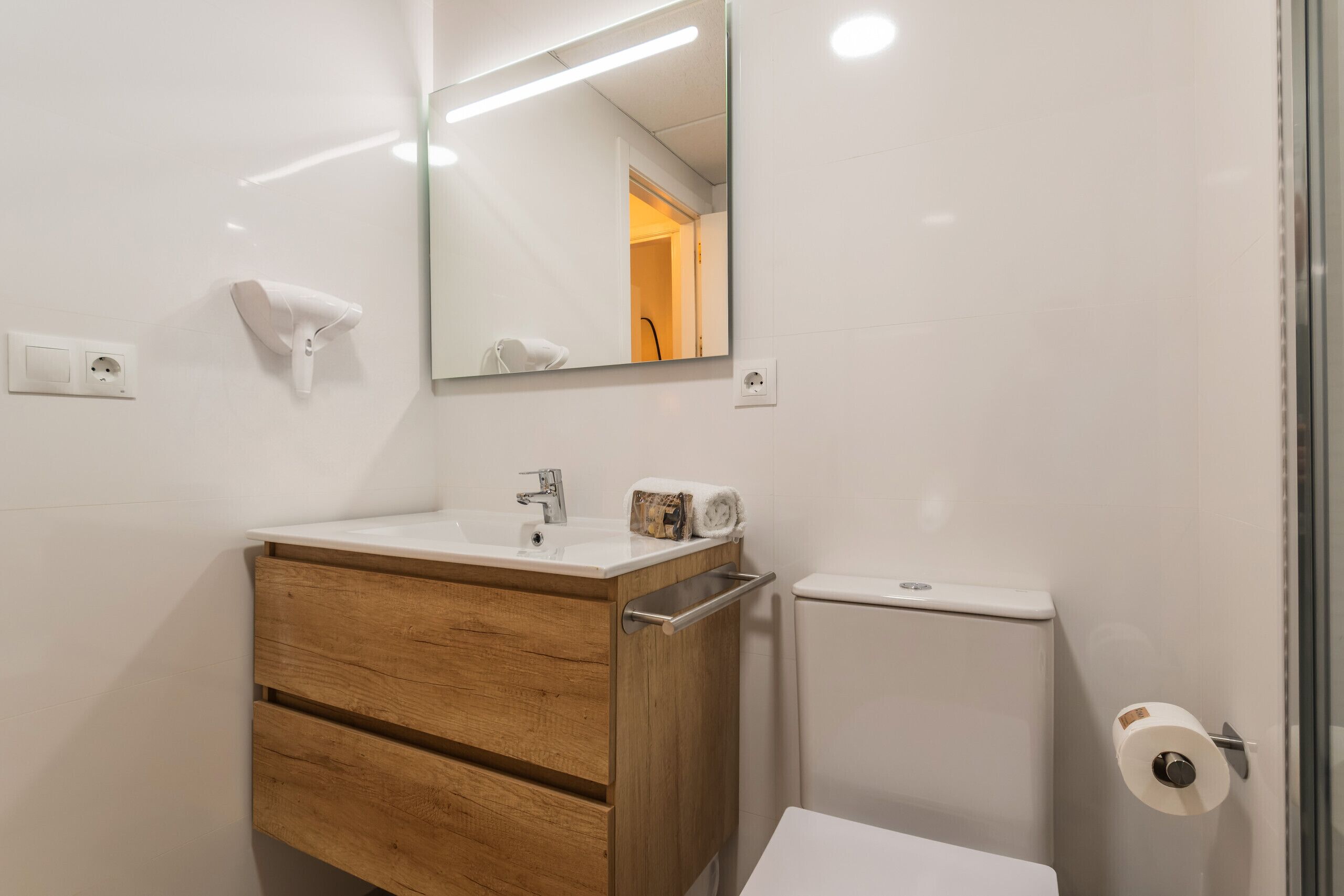 Une salle de bain avec un meuble-lavabo en bois, un miroir, des toilettes et un espace douche.