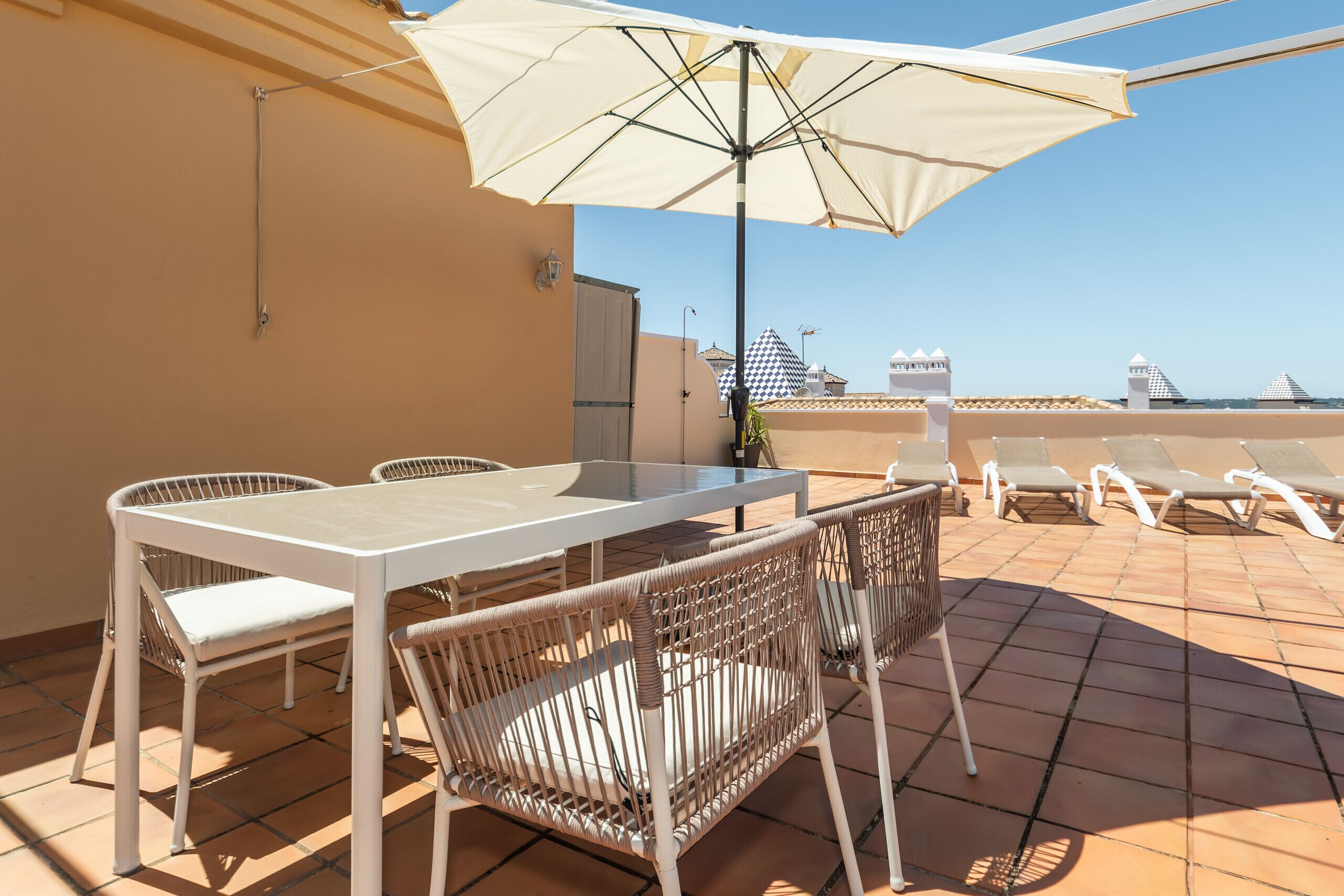 Une terrasse avec une table et des chaises, un parasol, et une vue sur les bâtiments en arrière-plan.