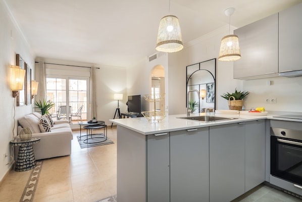 A modern kitchen with a central island, pendant lights, and a dining area with a sofa and chairs.