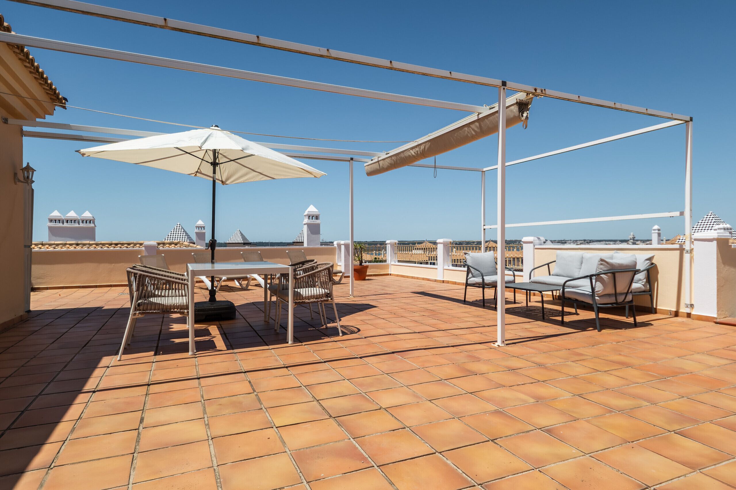 Una terraza con mesa y sillas, un paraguas blanco y vistas a edificios distantes.