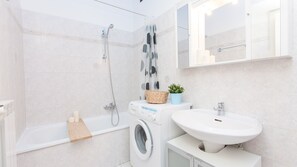 A modern bathroom with a built-in washing machine, a bathtub, a shower, a sink, and a mirror.