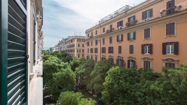 Une rangée de bâtiments européens traditionnels, caractérisés par des volets et des balcons de style uniforme, le tout entouré d’arbres verdoyants.