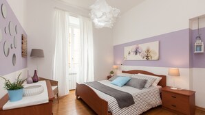 Une chambre à coucher avec un lit, des tables de chevet, une commode, une plante en pot et une fenêtre avec des rideaux.