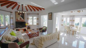 A spacious living room with a sofa, chairs, a TV, and a dining area with a table and chairs. - Gila - sea view villa with private pool in Benissa (Benissa)