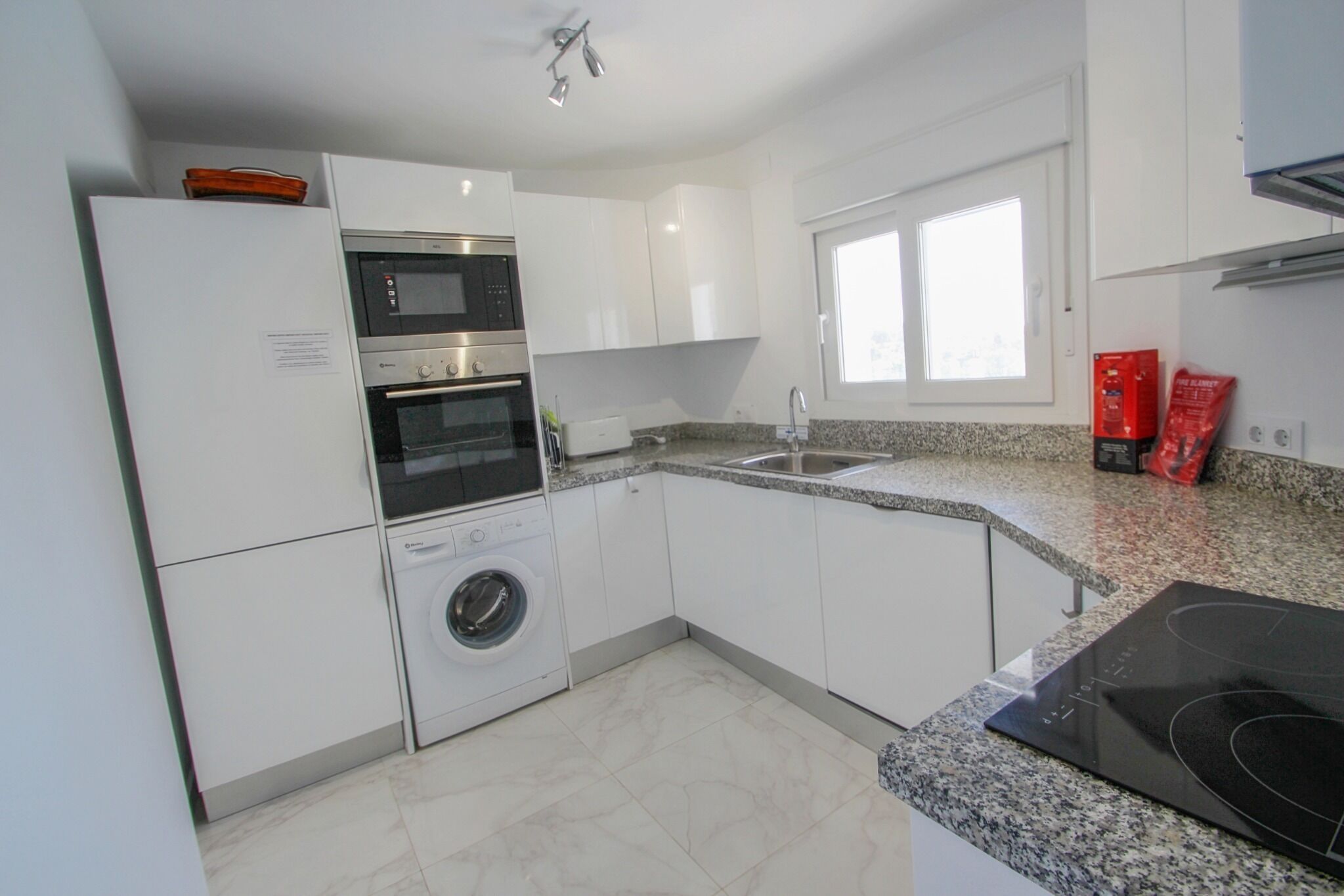 A modern kitchen with white cabinets, a built-in oven, microwave, and washing machine.