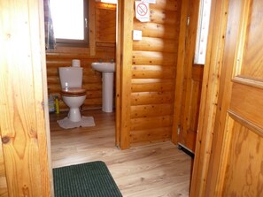 A wooden cabin bathroom with a toilet, sink, and a 'no smoking' sign.