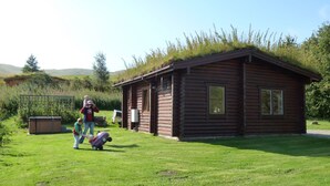 A wooden cabin with a thatched roof, surrounded by a grassy yard and a wooden fence. - Log Cabin with Hot Tub for 2 | In the Cairngorm National Park | Accepts Dogs (Spittal of Glenshee)