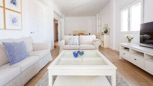 Een moderne woonkamer met een witte bank, een glazen salontafel en een televisie op een witte kast.