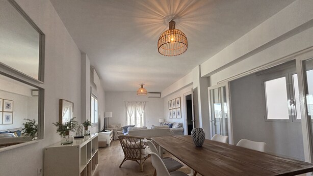 Een ruime woonkamer met een lange houten tafel, witte stoelen en een hanglamp.