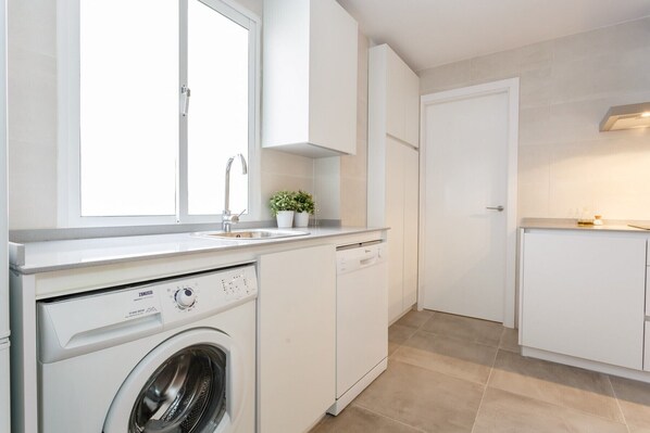 Une cuisine moderne équipée d’un lave-linge encastré, d’un évier et d’une fenêtre.