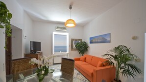 A living room with a large window, a sofa, a TV, and a potted plant. - Casa Sunset - Panoramic terrace overlooking Positano and Capri (Praiano)