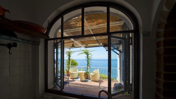 A bathroom with a large arched window overlooking a patio with outdoor furniture and a view of the sea. - Casa Sunset - Panoramic terrace overlooking Positano and Capri (Praiano)