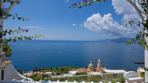 A coastal view with a clear sky, a body of water, and a building with a dome and bell tower. - Casa Sunset - Panoramic terrace overlooking Positano and Capri (Praiano)