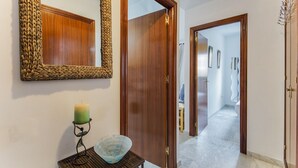 Un pasillo con puertas de madera, un espejo con marco trenzado, un candelabro y un cuenco sobre una mesita.