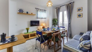 Una sala de estar moderna con comedor, que incluye una mesa de madera, sillas azules, un sofá y un televisor en la pared.