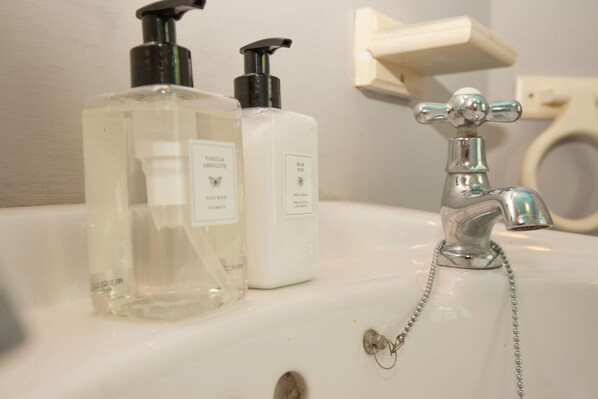 A bathroom sink with two bottles of hand soap and a faucet with a chain.