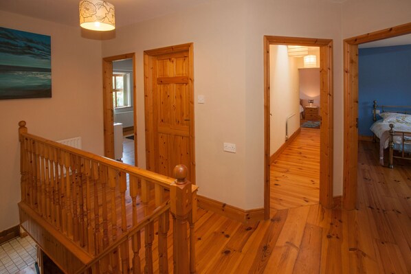 Un escalier en bois avec une rampe, menant à une chambre à coucher équipée d’un lit et d’une table de chevet.