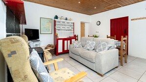 A cozy living room with a sofa, wooden chairs, a television, and a red cabinet with kitchenware. - Cottage 194 - Leenane - sleeps 4 guests  in 2 bedrooms (Leenane)