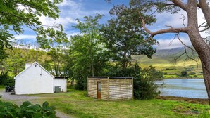 A rustic cabin with a small shed, surrounded by lush greenery and a lake. - Cottage 194 - Leenane - sleeps 4 guests  in 2 bedrooms (Leenane)