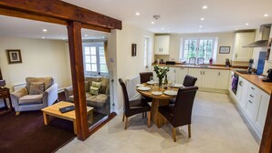 A modern kitchen with white cabinets, a dining area with a wooden table and chairs, and a cozy living room with a sofa and armchair. - A sudeley castle cottage that sleeps 4 guests  in 2 bedrooms (Winchcombe)