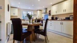 A modern kitchen with white cabinets, a wooden dining table, and two black leather chairs. - A sudeley castle cottage that sleeps 4 guests  in 2 bedrooms (Winchcombe)