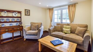 A living room with a sofa, armchair, wooden coffee table, and a sideboard with decorative plates. - A sudeley castle cottage that sleeps 4 guests  in 2 bedrooms (Winchcombe)