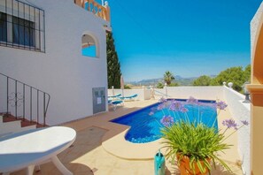 Zona de piscina con piscina azul, sillones de descanso y una planta en maceta.